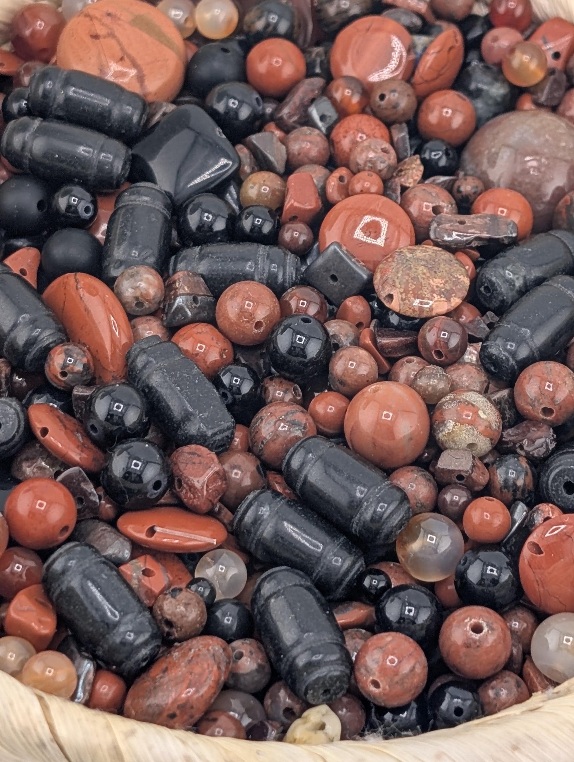a close-up view of a collection of various beads and stones, including black, red, and orange beads, as well as some larger stones. The objects are scattered and overlapping, creating a visually interesting and diverse composition.