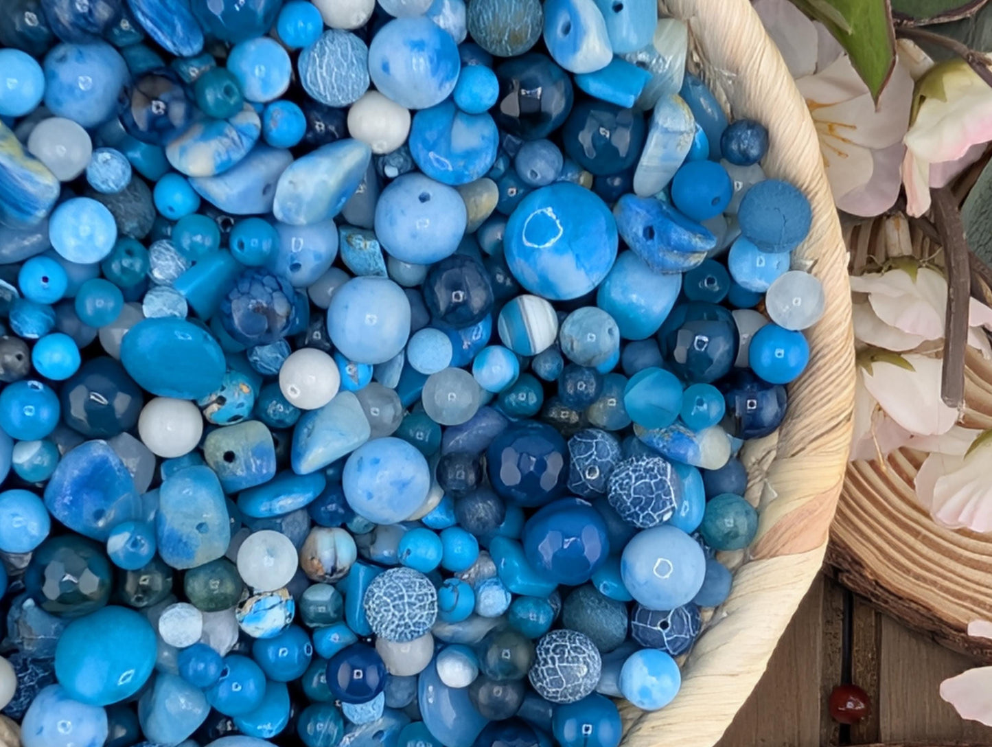 A basket filled with various blue beads, including blue and white beads, and some white flowers.