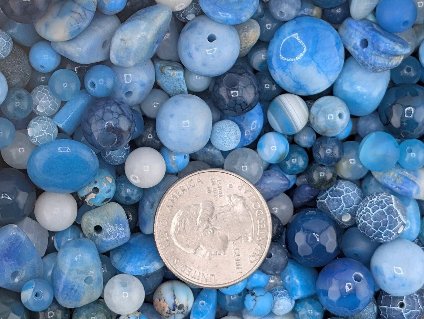 a collection of various blue beads and stones, with a silver coin placed in the center to provide a scale reference.