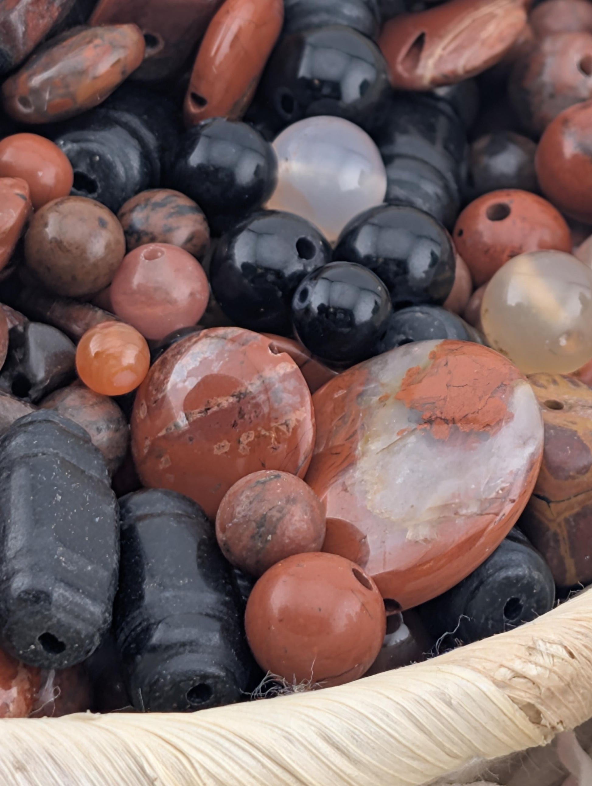 A close-up image of various colorful beads and stones, including black, orange, and white beads, arranged in a basket.