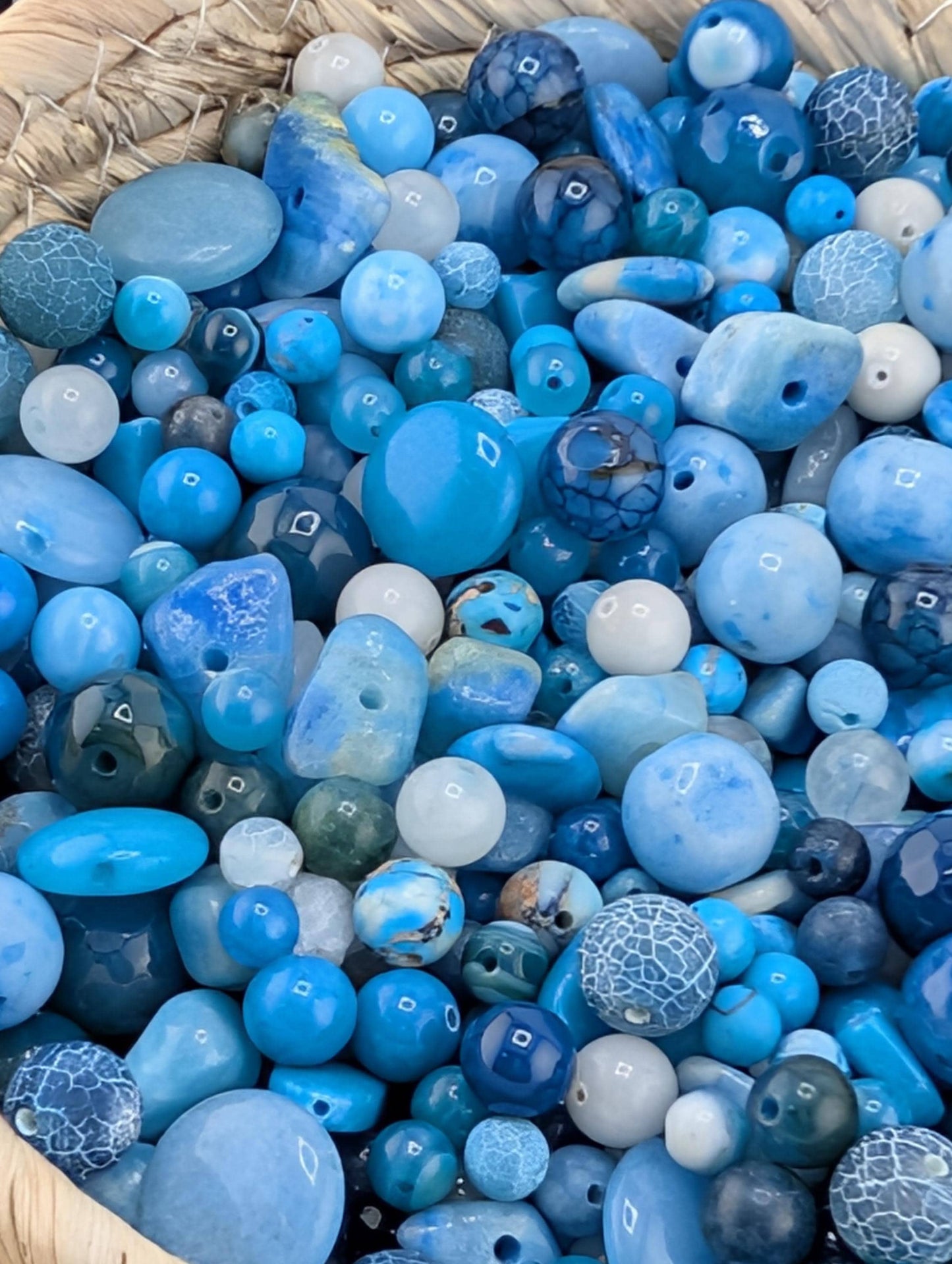 The image is a close-up of a collection of various blue and white beads, including glass beads and stone beads, arranged in a basket.