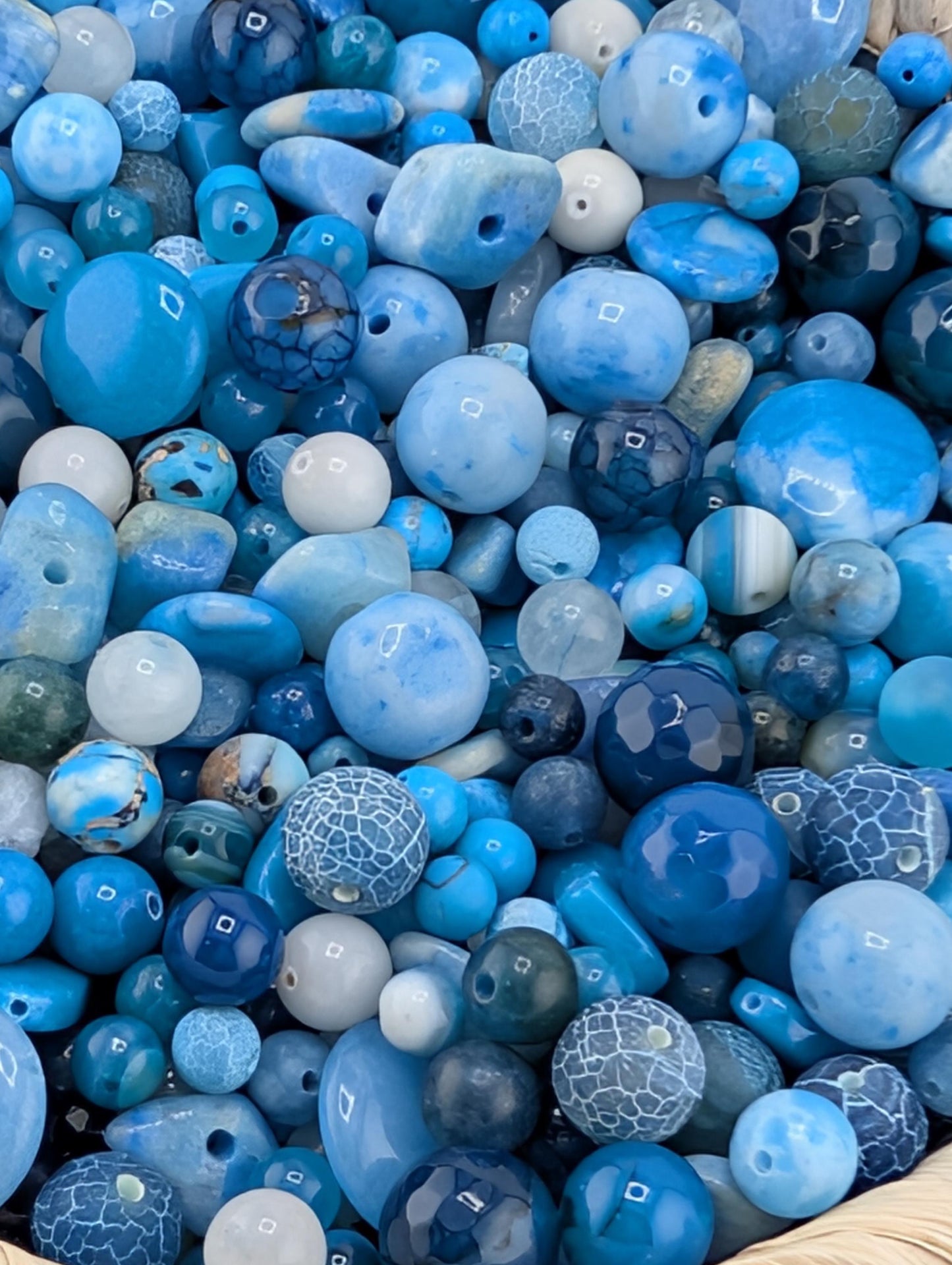 The image is a close-up of a collection of various blue and white beads, including glass beads and stone beads, arranged in a visually appealing manner.