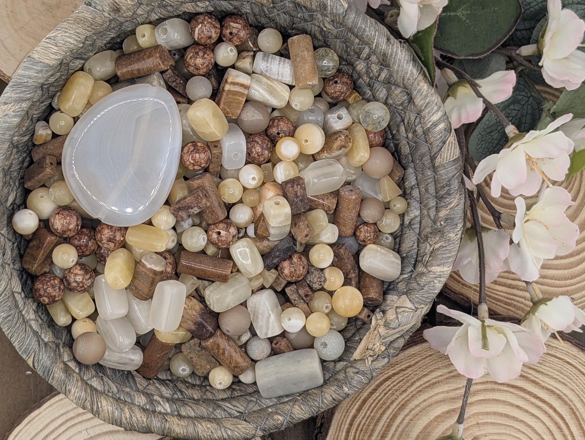 A woven basket filled with various beads and stones, including white, brown, and beige colors, along with some flowers.