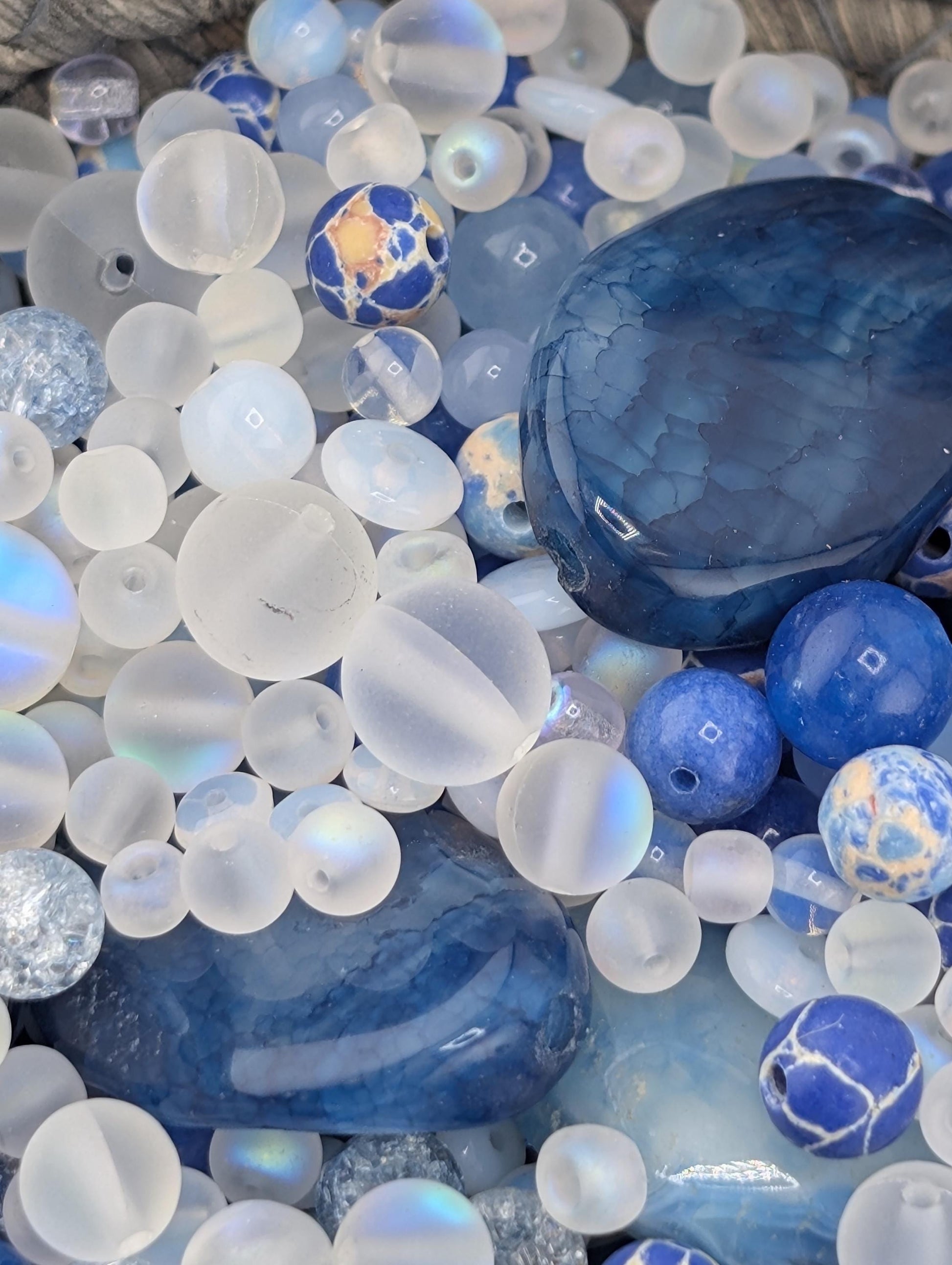 The image is a close-up of various glass beads and stones, including clear, blue, and white beads, as well as some larger stones.