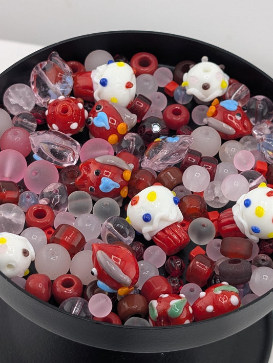 A black bowl filled with a variety of colorful glass beads, including red, white, and multicolored beads, as well as some with polka dots and other playful designs.