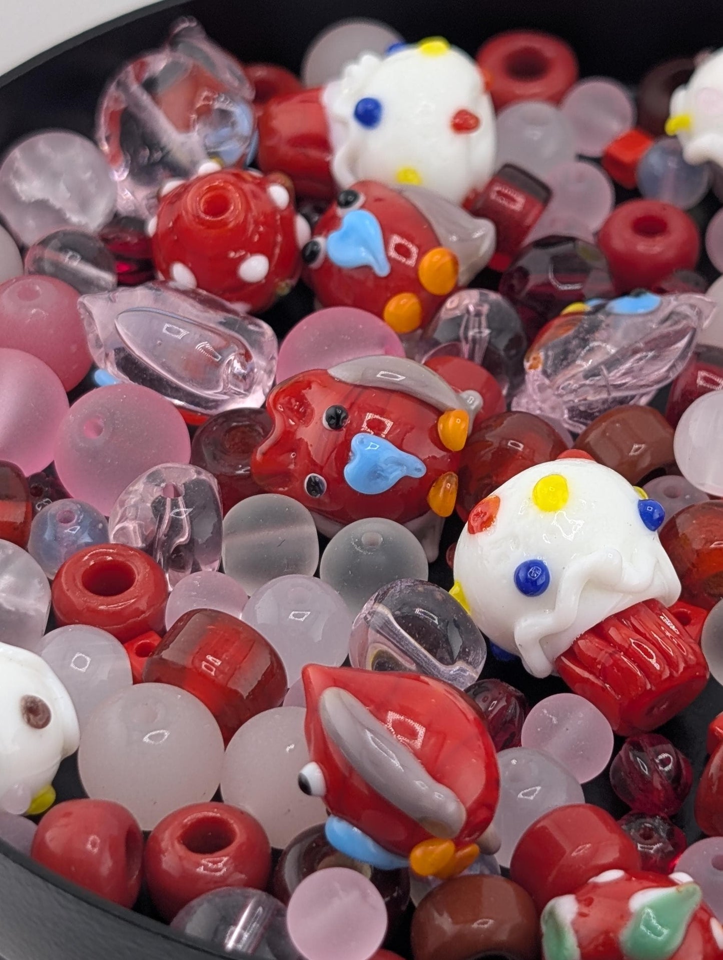 a collection of colorful glass beads and objects, including small red and white beads, clear beads, and other glass items with various shapes and designs.