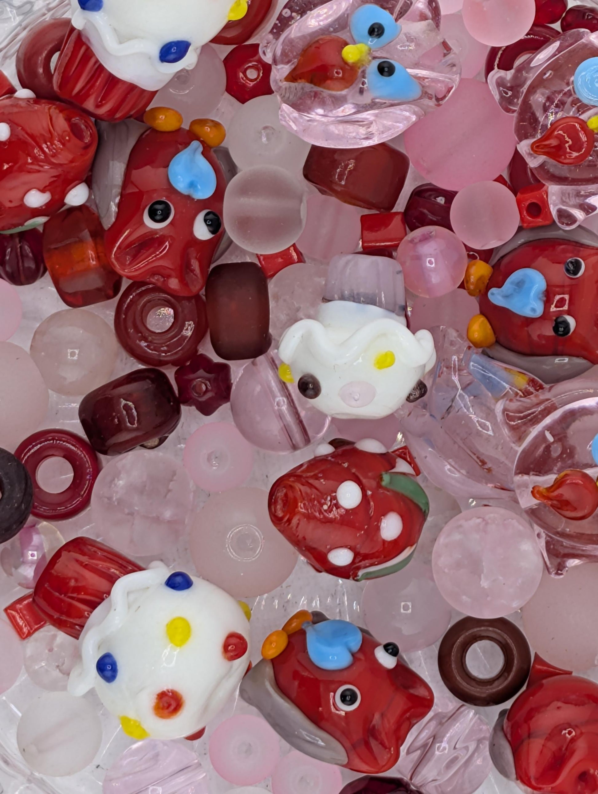 The image is a colorful assortment of various glass beads and candies, including small red and white beads, clear beads, and some with colorful designs.