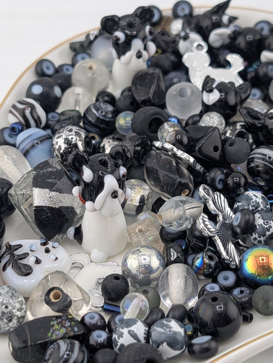 a variety of black and white beads, glass beads, and small figurines, including a dog figurine, arranged on a white surface.