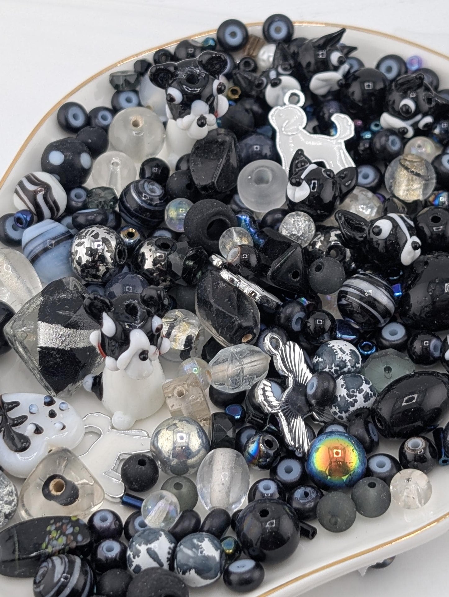 The image is a collection of various beads and objects in shades of black and white, including glass beads, metal beads, and other decorative items.