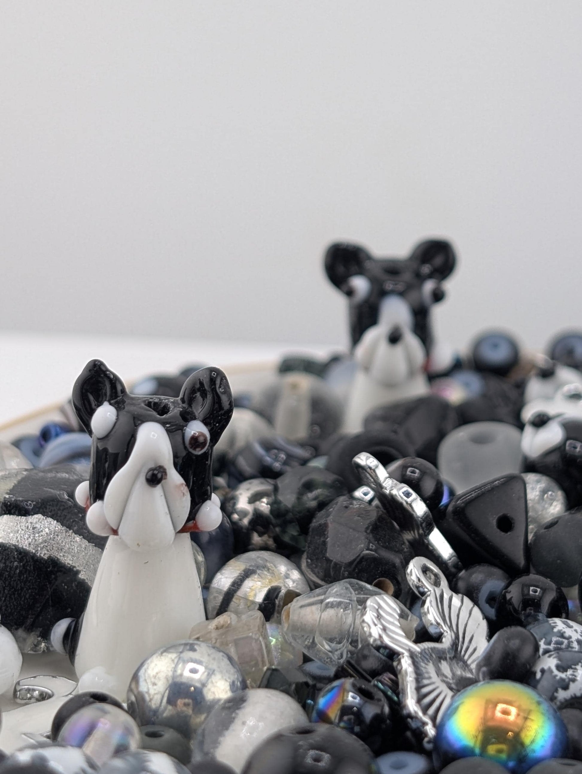 two black and white dog figurines surrounded by various beads and glass objects, creating a visually interesting and playful composition.