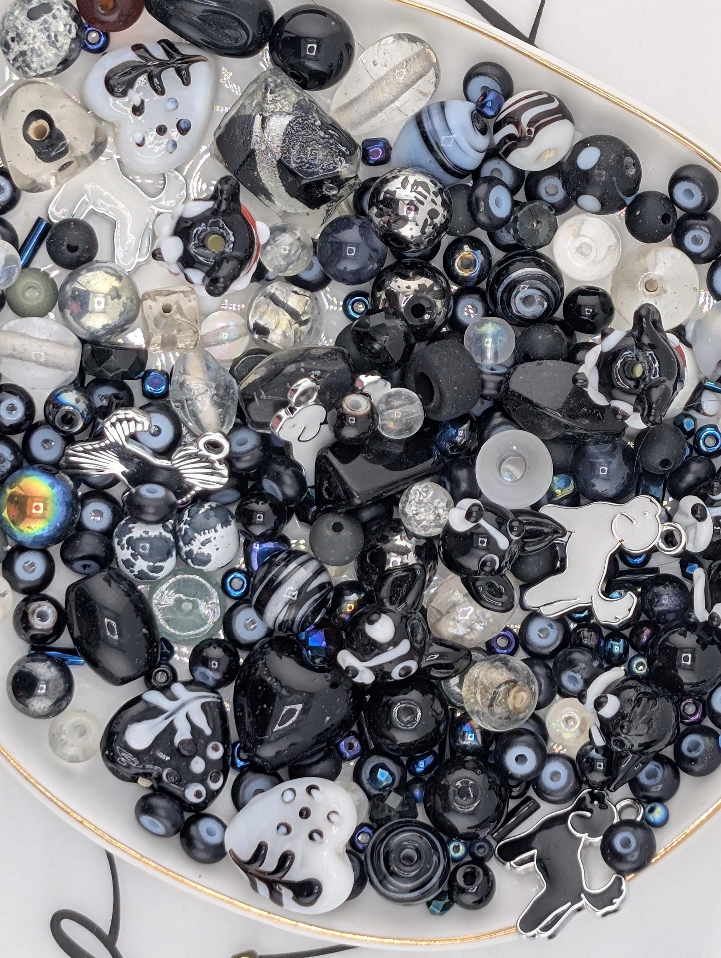 The image is a collection of various black and white beads, charms, and glass beads arranged on a white surface.