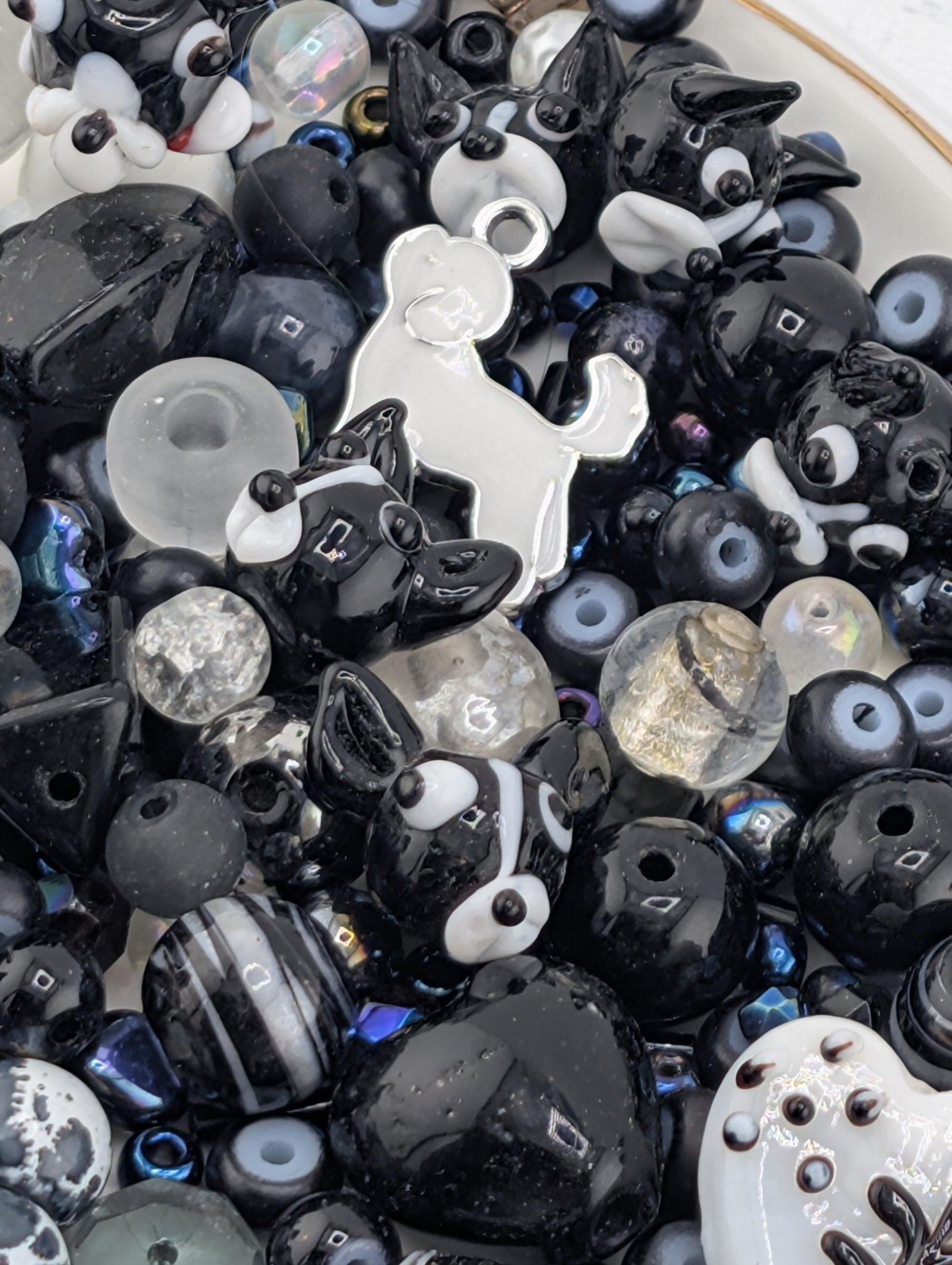 The image is a close-up of a collection of various beads and charms, including black and white beads, glass beads, and small figurines.