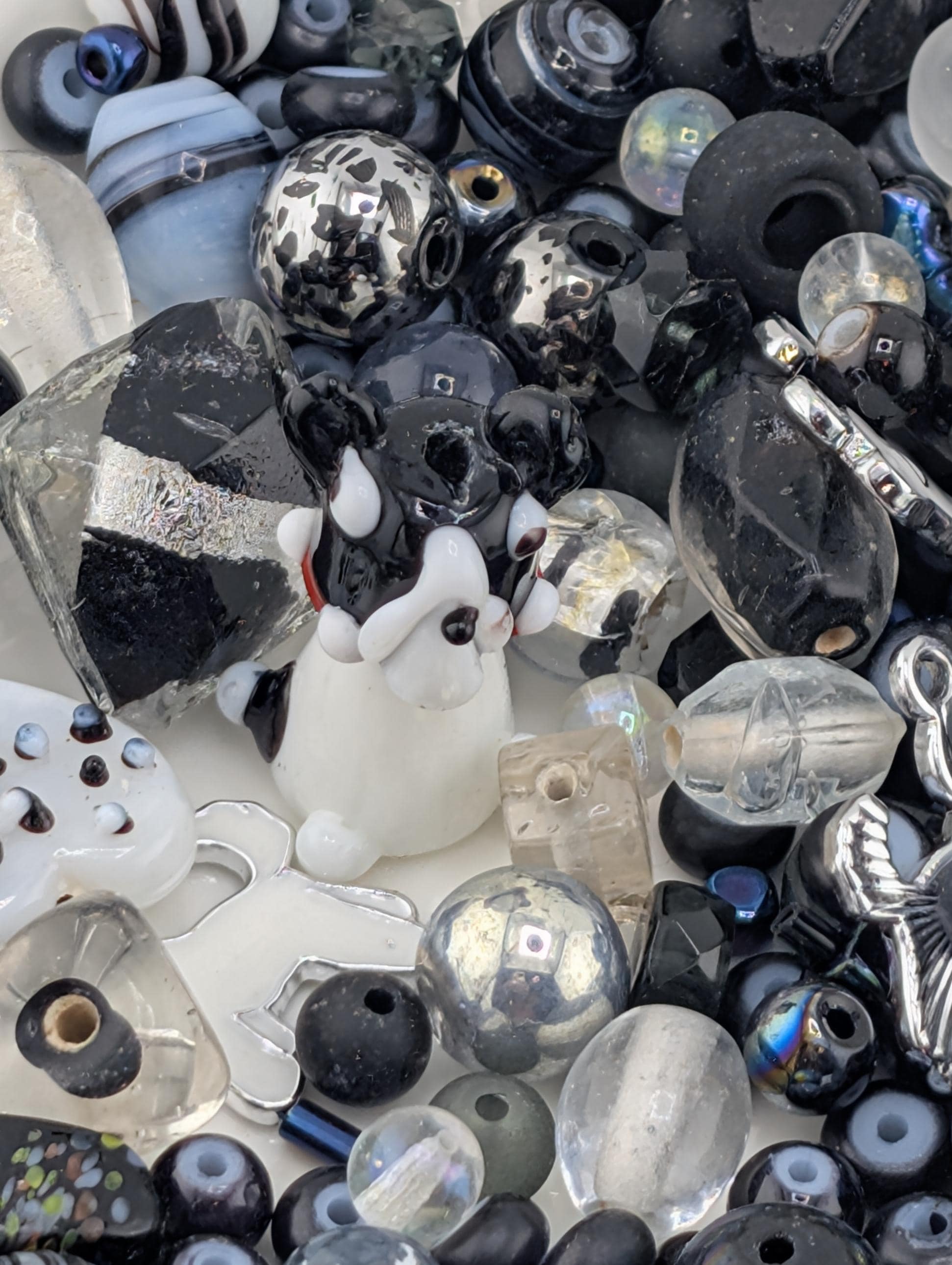 The image is a collection of various glass beads and objects, including a small glass dog figurine, arranged in a visually interesting manner.