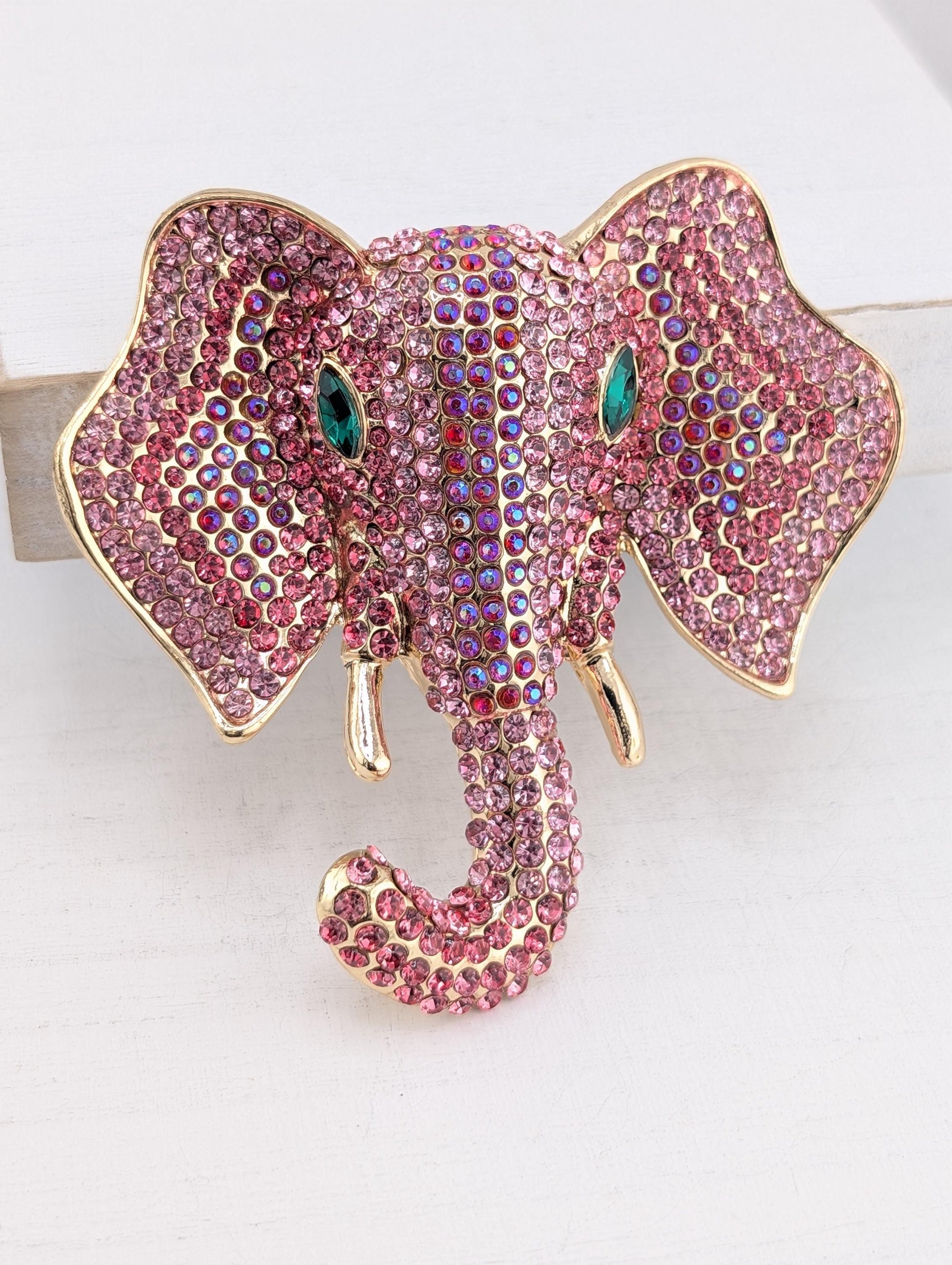A decorative elephant head brooch made of pink and purple rhinestones, with gold accents.