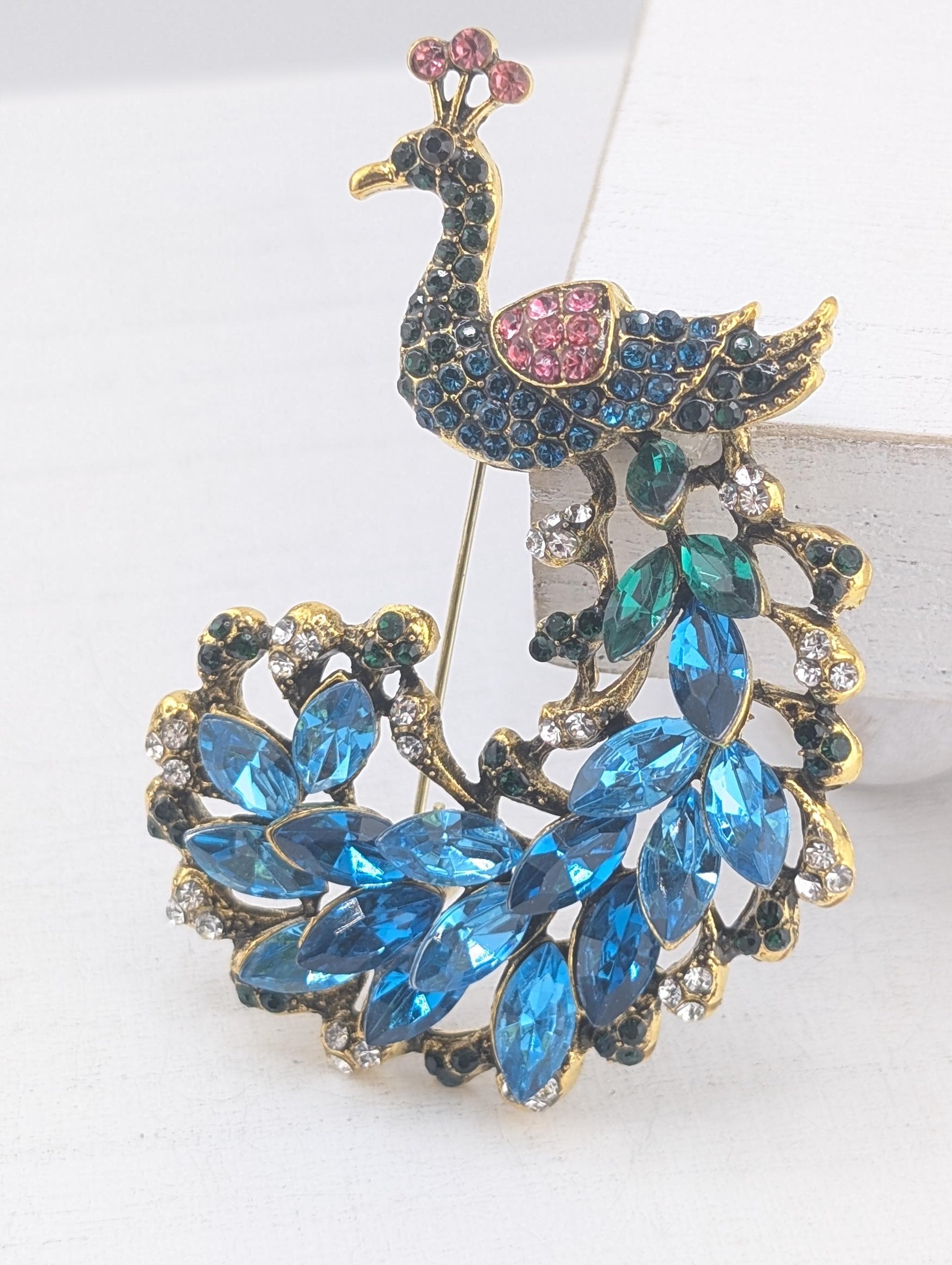 A decorative brooch in the shape of a peacock, adorned with blue and pink gemstones.