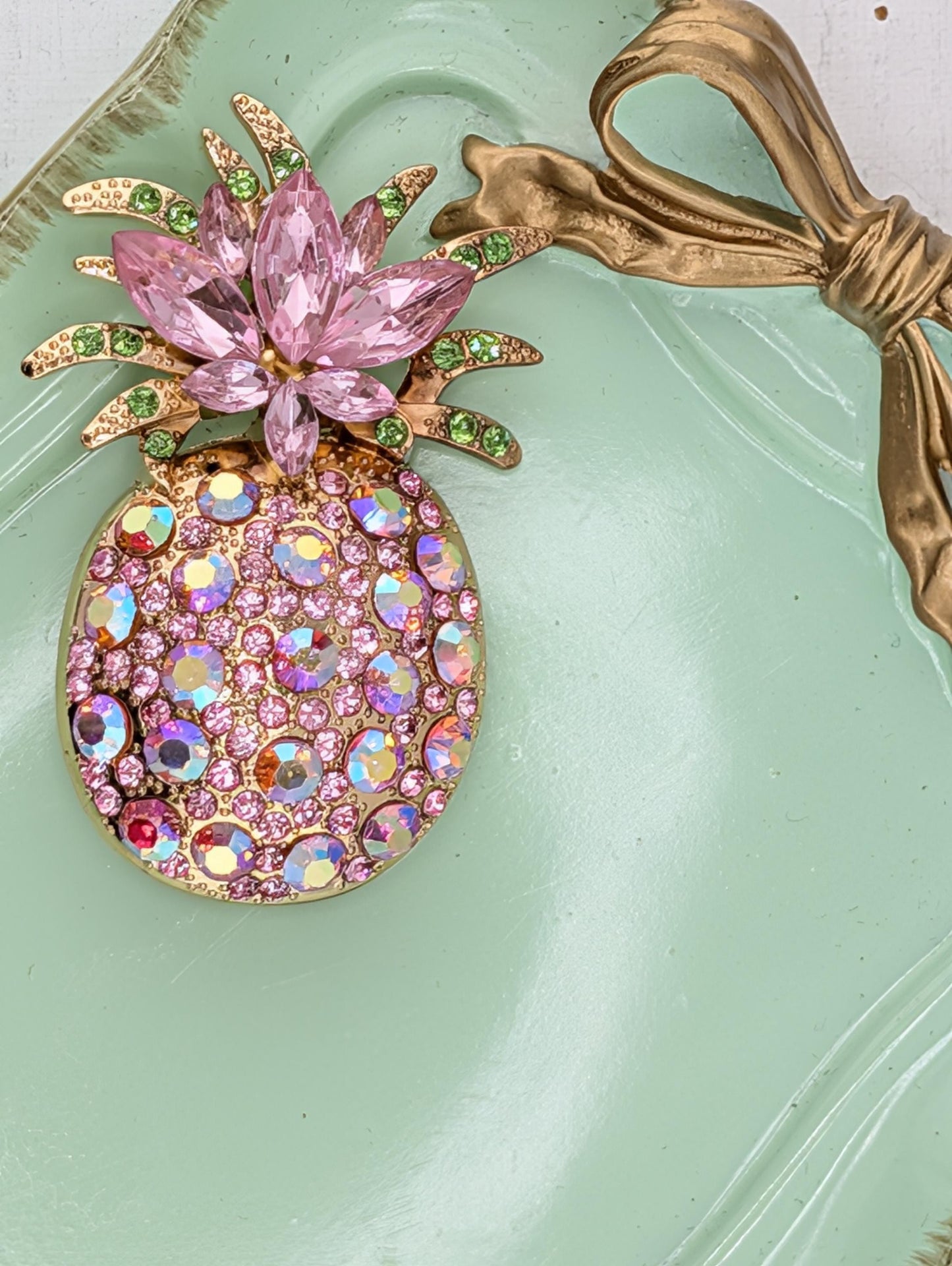 A decorative pineapple-shaped brooch adorned with pink crystals and a gold bow.