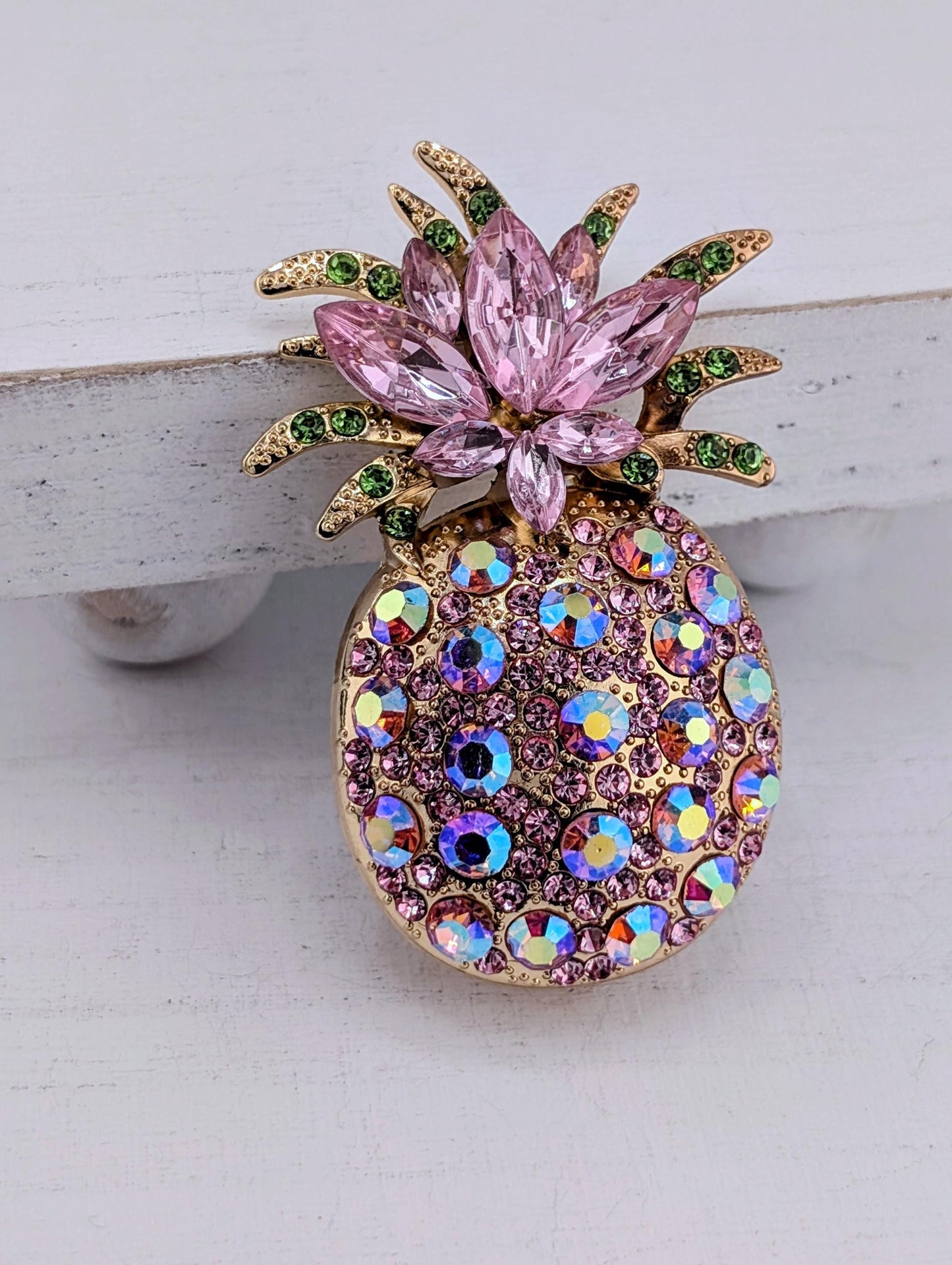 A decorative pin featuring a pineapple design with pink and green gemstones.
