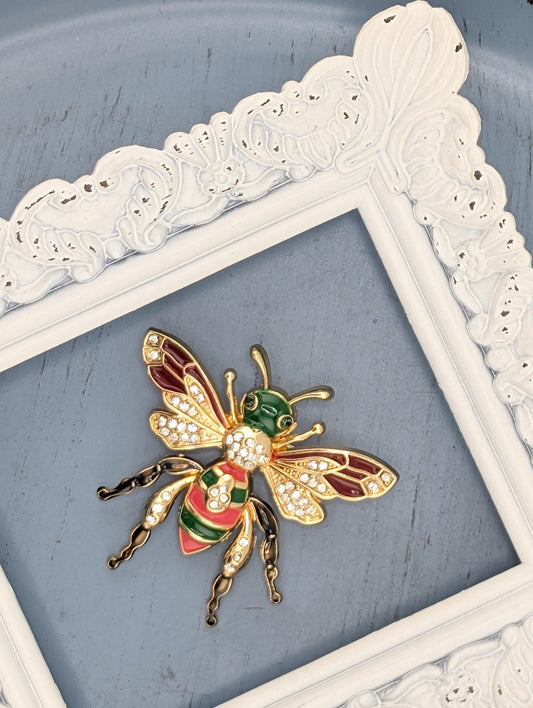 A decorative white frame with a gold and green bee brooch on a blue background.