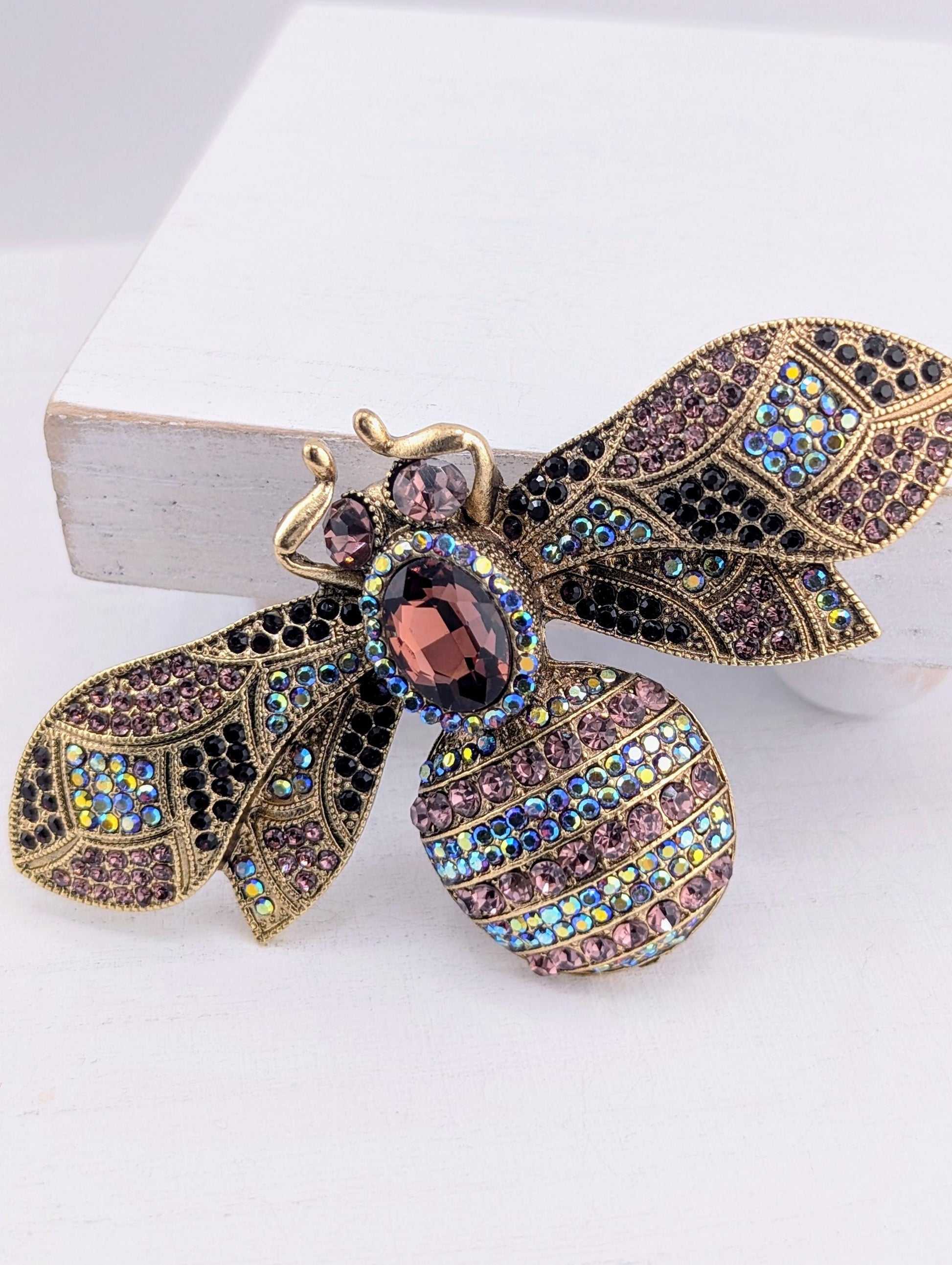 A decorative brooch in the shape of a bee, adorned with colorful gemstones and intricate details.