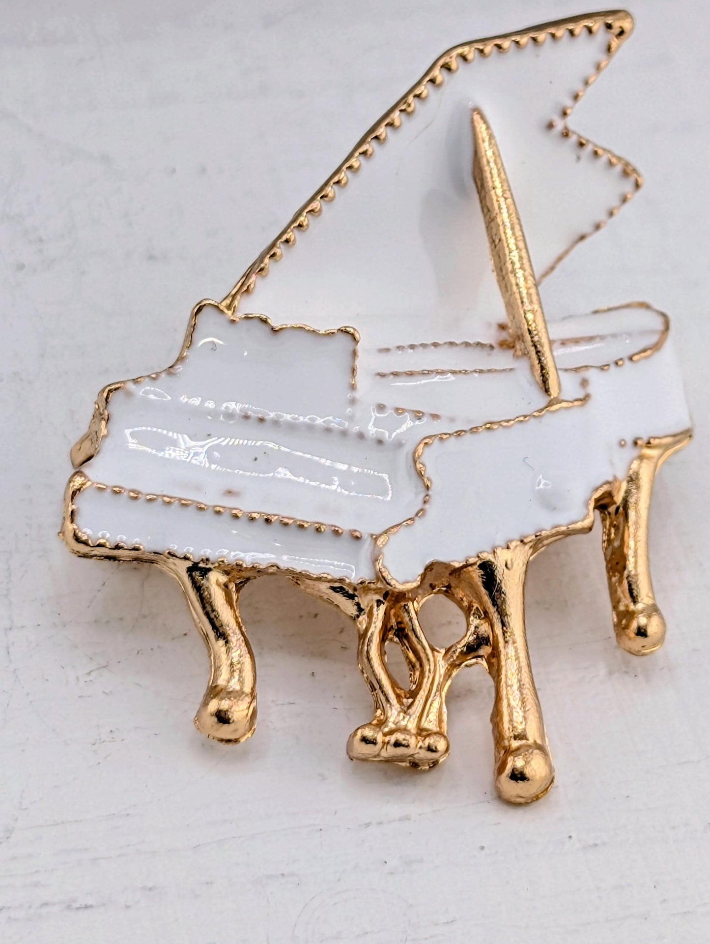 A white and gold piano brooch with a gold piano key and gold piano leg.