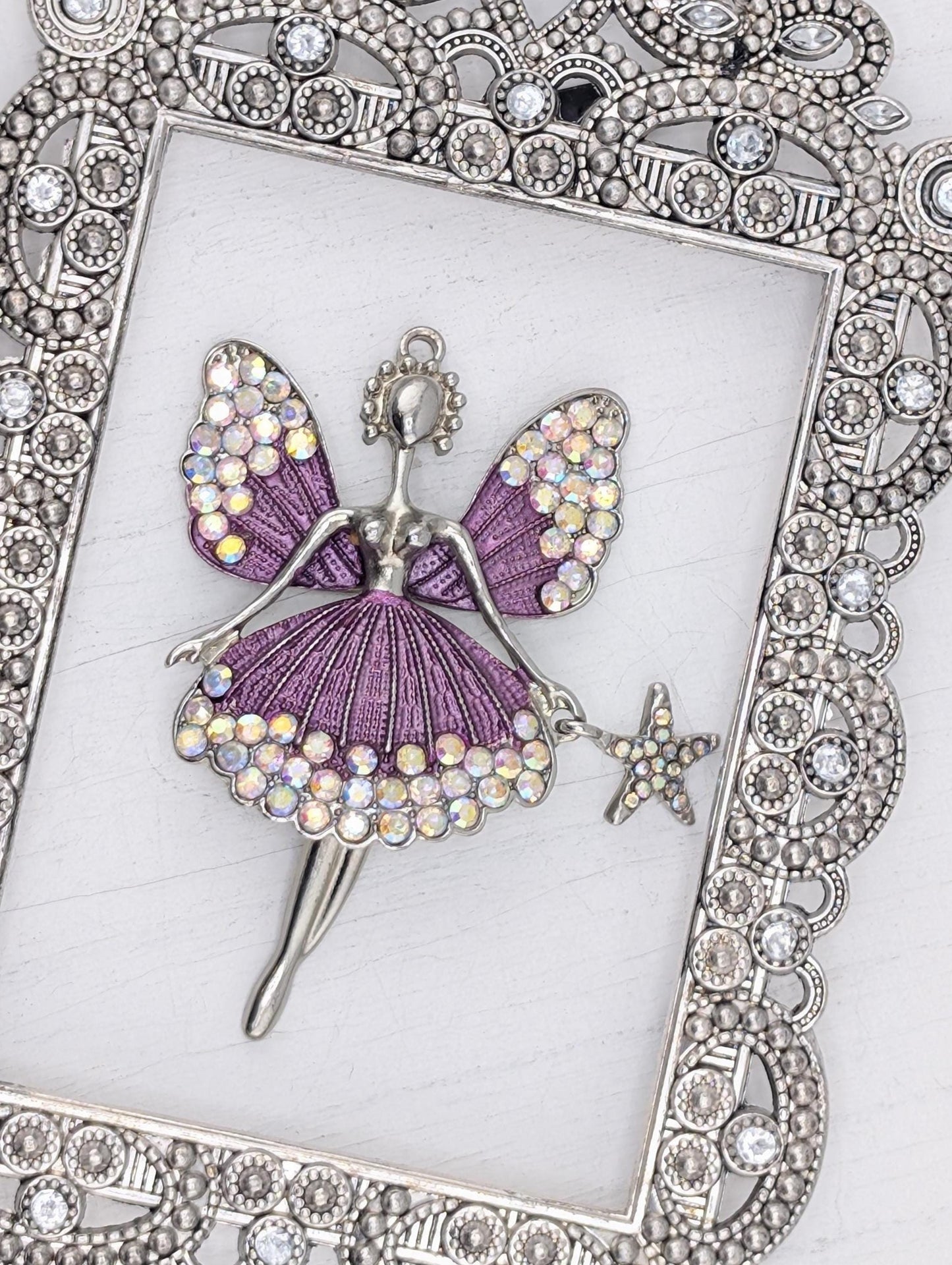 A silver-colored frame with a decorative border, containing a purple butterfly-shaped pendant with a star-shaped charm.