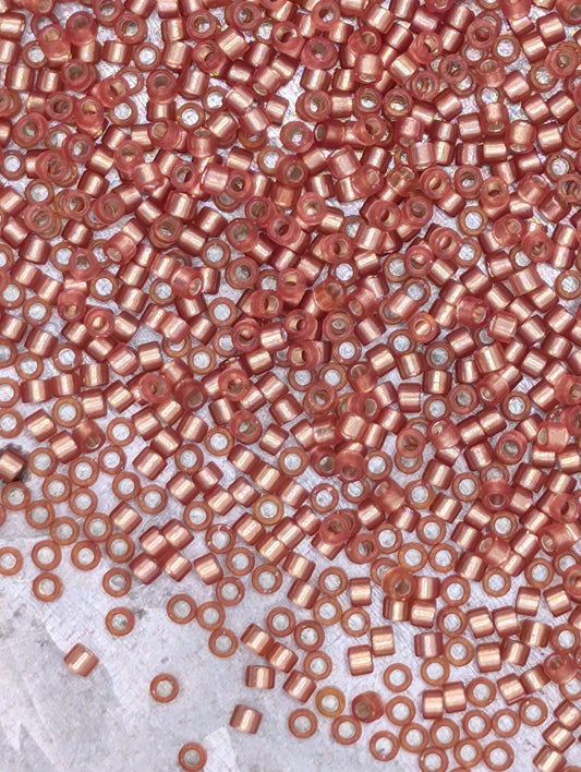 The image is a close-up of numerous small, round, metallic beads in a variety of colors, including shades of red, orange, and pink. The beads are scattered across a surface, creating a visually striking and vibrant display.