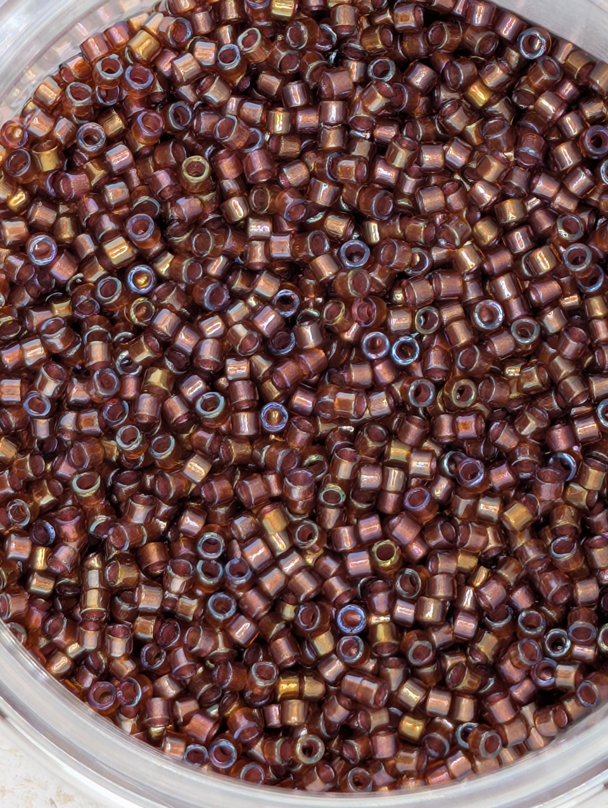 A close-up image of a container filled with numerous small, round beads in various shades of brown and gold.