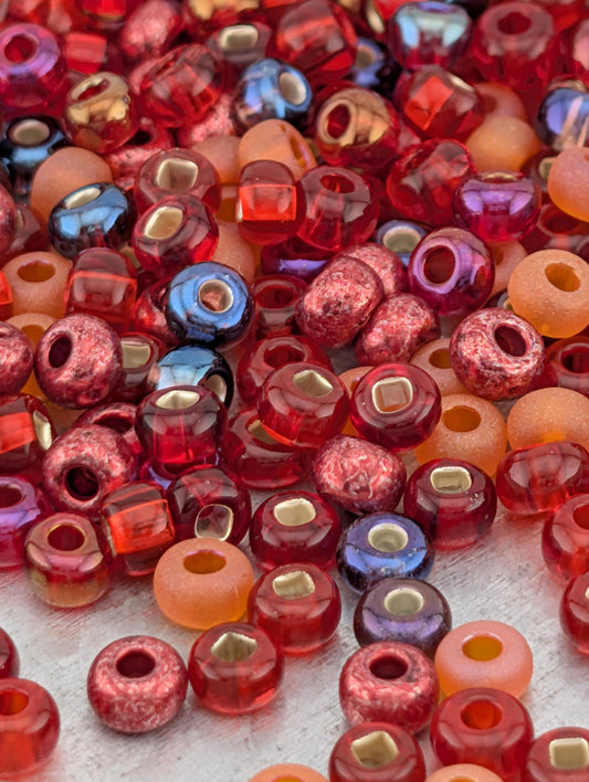 The image is a close-up of a pile of colorful glass beads, including red, orange, and purple beads, scattered on a surface.