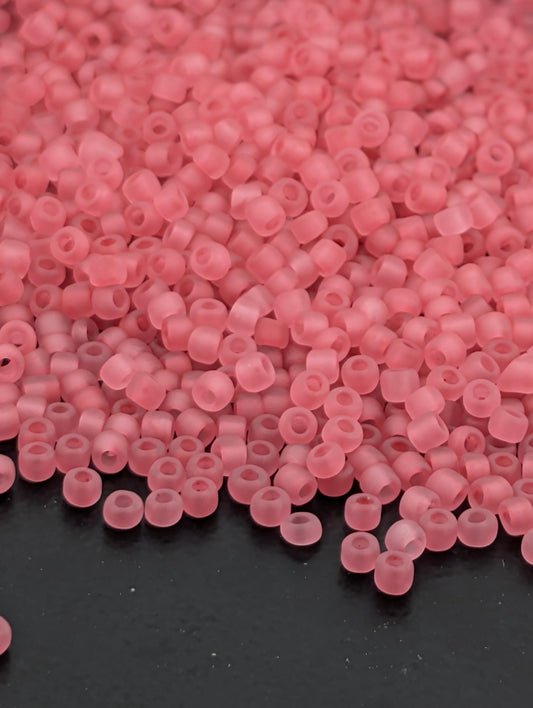 a close-up view of numerous small, clear beads in a soft pink color, scattered across a dark surface.