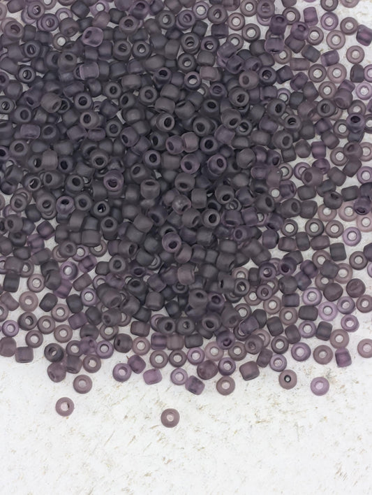 a large pile of small, round beads in various shades of purple, scattered on a white surface.