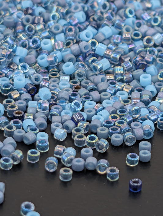 a large pile of small, clear beads in various shades of blue and gray, scattered on a dark surface.