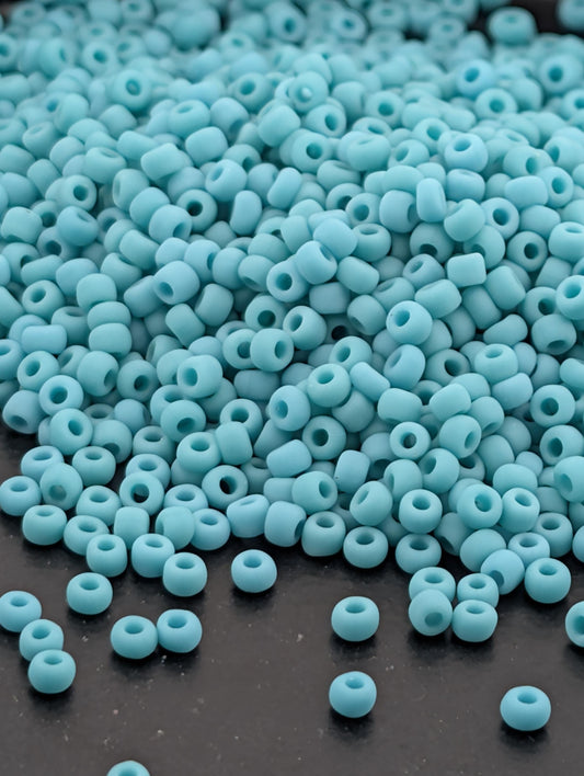 A pile of small, light blue beads scattered on a dark surface.