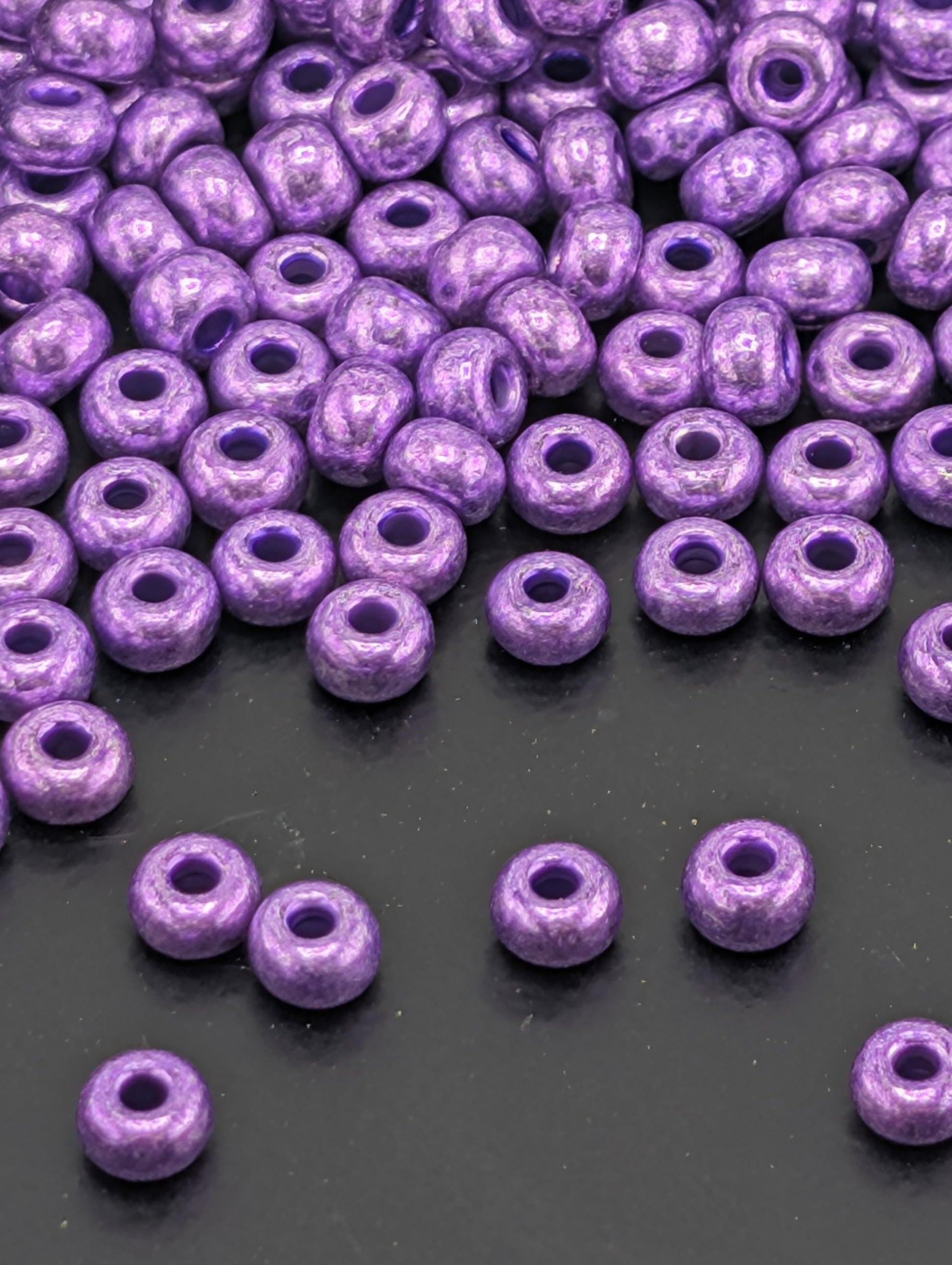 a collection of purple beads scattered on a dark surface, with some of the beads overlapping each other.