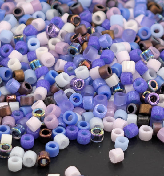 A pile of multicolored beads, including white, purple, blue, and brown, scattered on a dark surface.