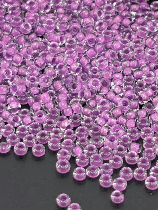 a close-up view of numerous small, clear beads in shades of purple, scattered across a dark background.
