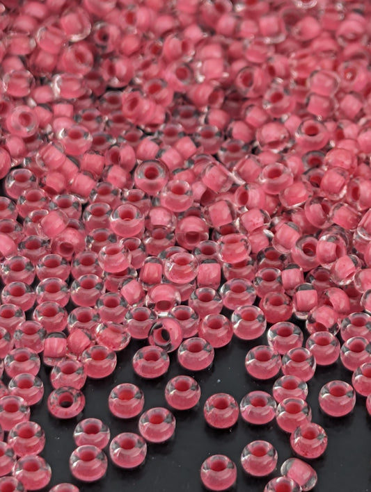 The image is a close-up of numerous clear glass beads in a pink color, scattered across a dark background.