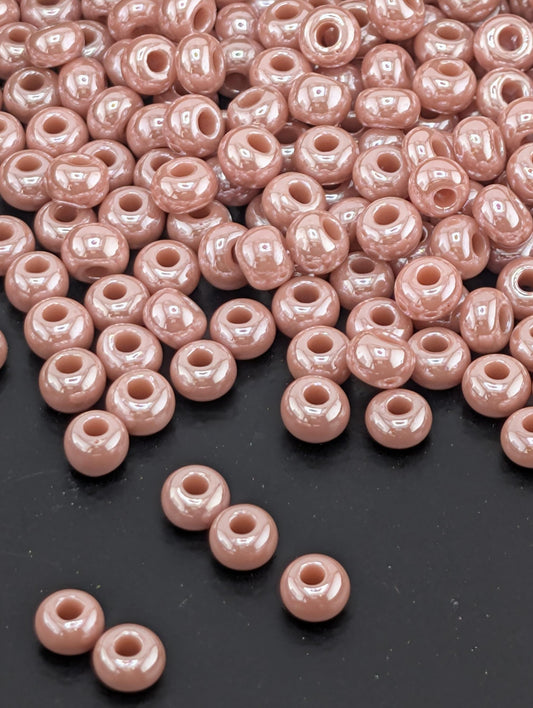 a large pile of small, round, pink beads scattered on a dark surface.
