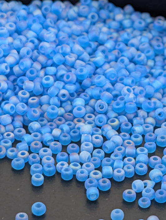 a large pile of small, clear blue beads scattered on a dark surface.