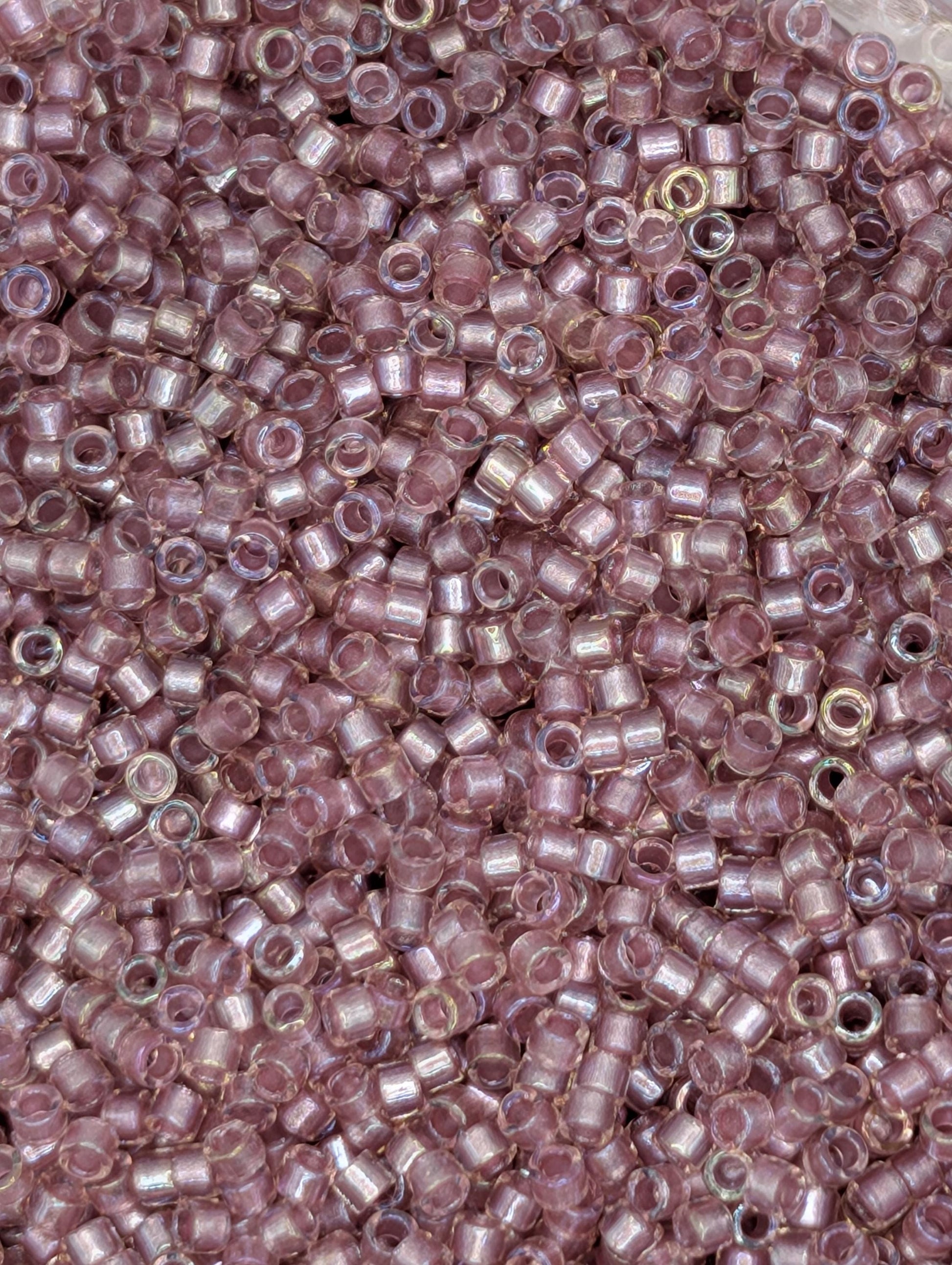 The image is a close-up of numerous small, round beads in shades of pink and purple.