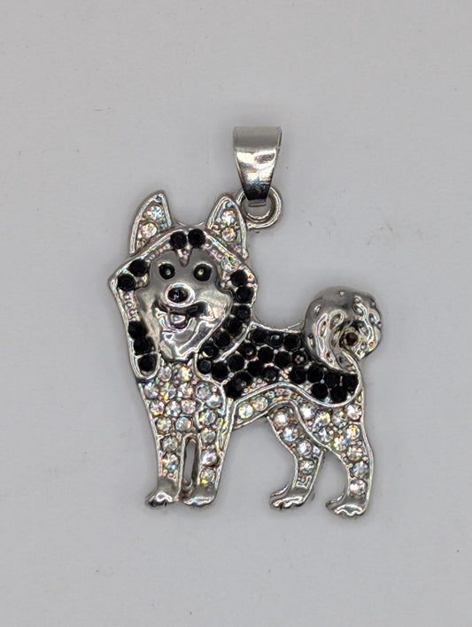 A silver-colored pendant in the shape of a dog, adorned with black and white rhinestones or crystals.