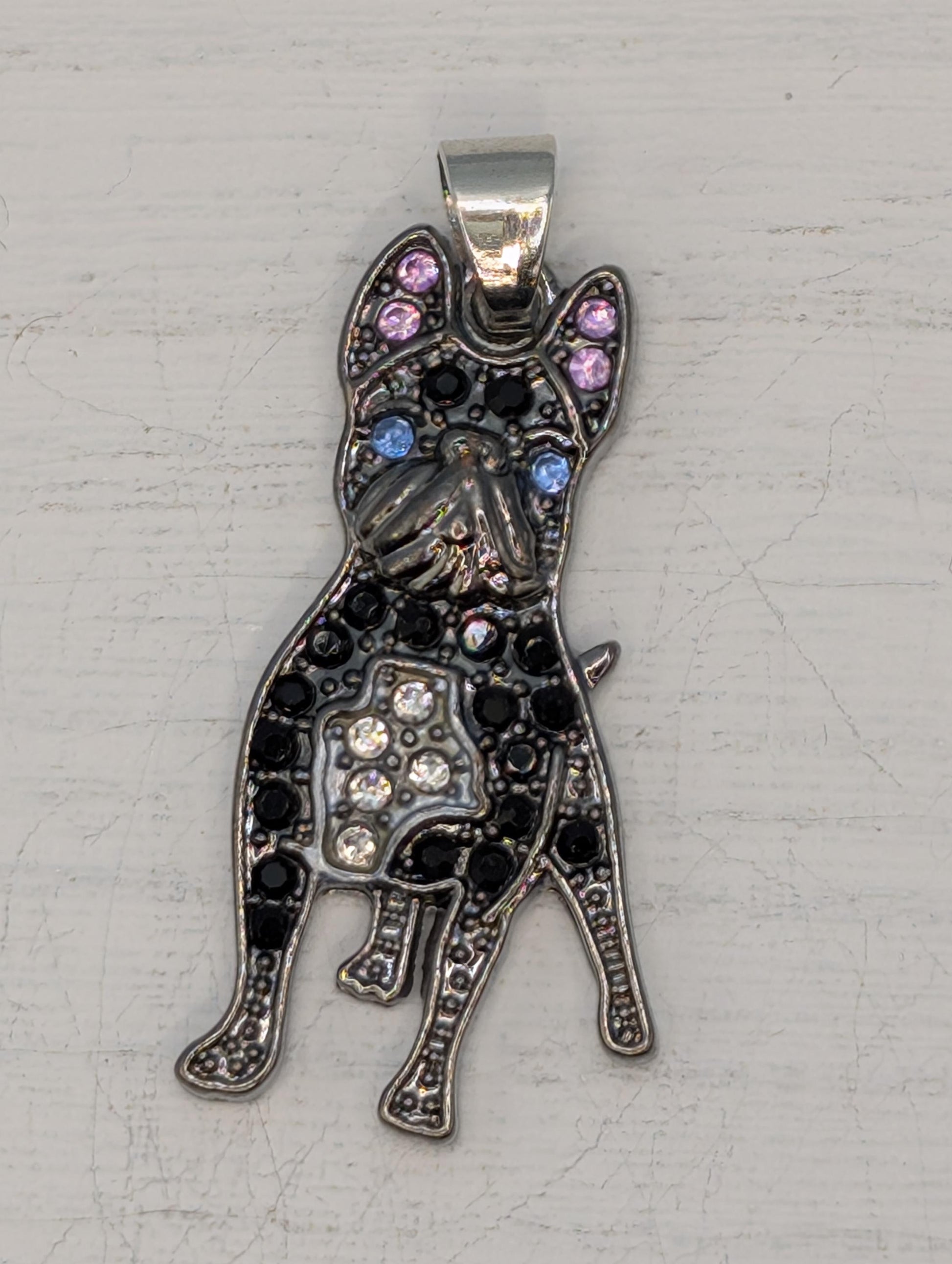 A decorative pendant in the shape of a dog, with a metallic appearance and adorned with small gemstones or crystals.