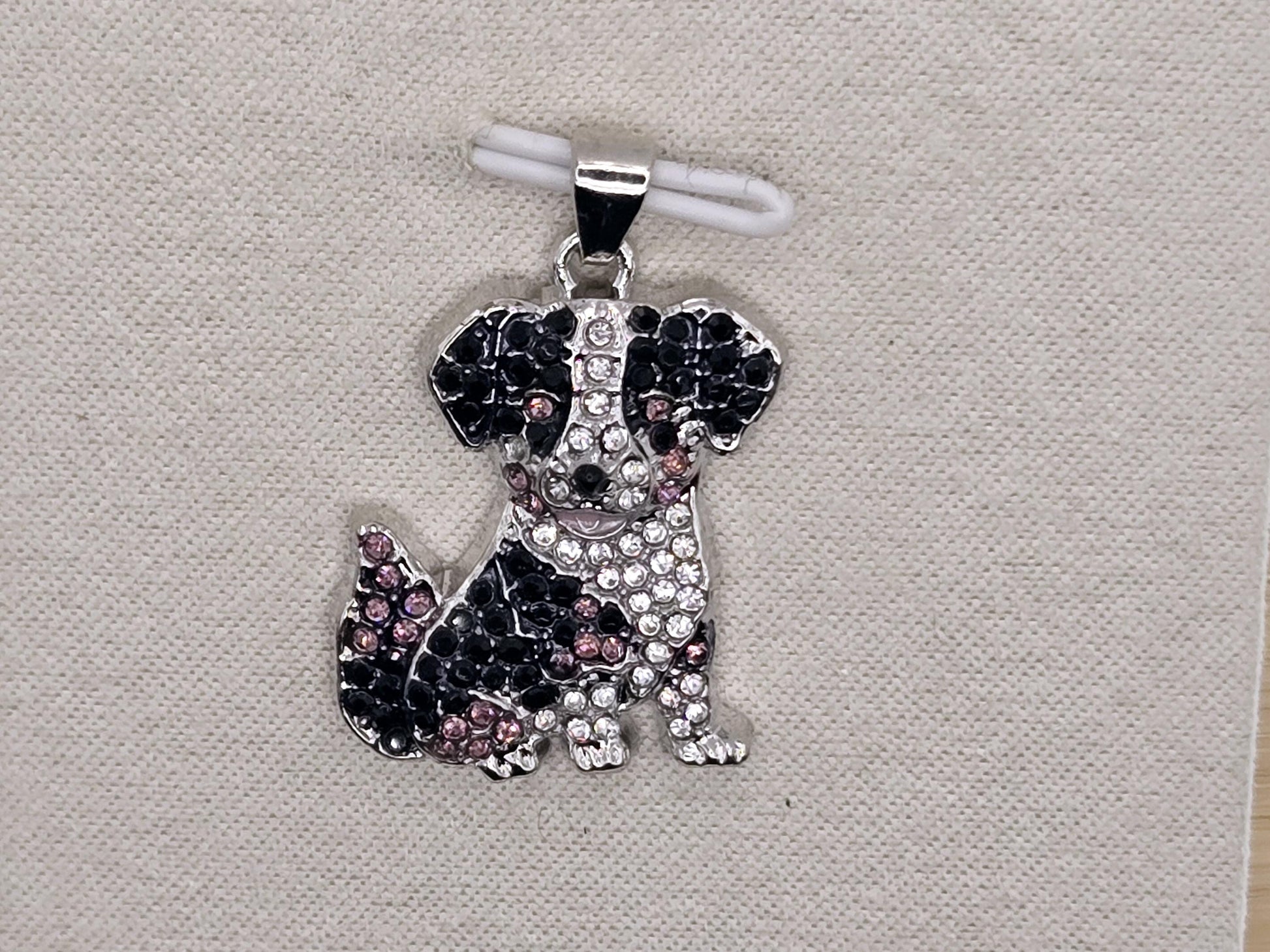 A silver-toned pendant in the shape of a dog, adorned with sparkling rhinestones and colored gemstones.