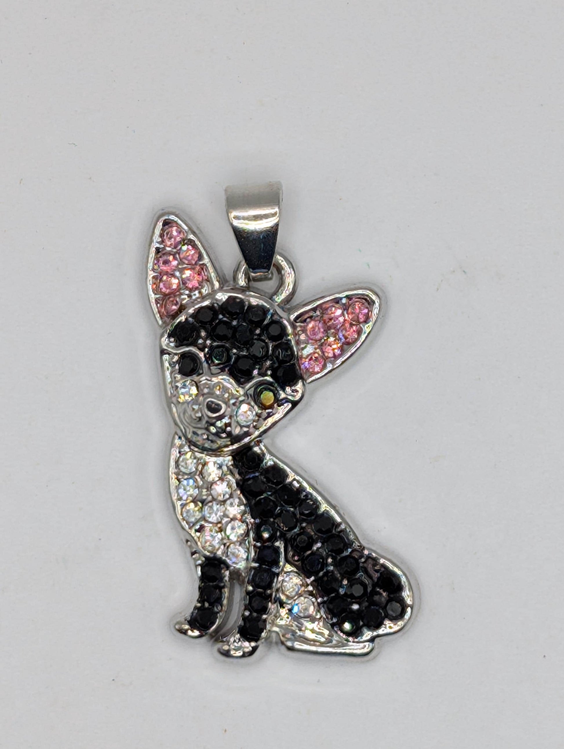 A silver-colored pendant in the shape of a dog, adorned with black and pink rhinestones or crystals.