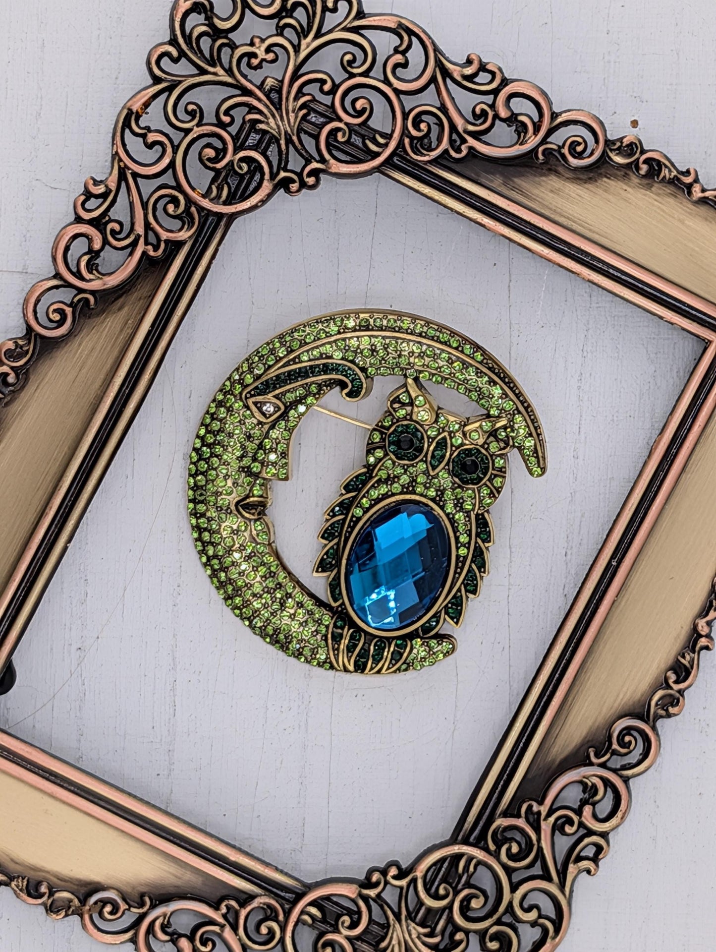 a decorative brooch with a moon-like design and a blue gemstone, displayed within an ornate gold frame.