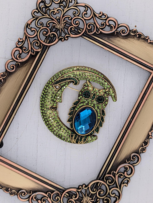 a decorative brooch with a moon-like design and a blue gemstone, displayed within an ornate gold frame.