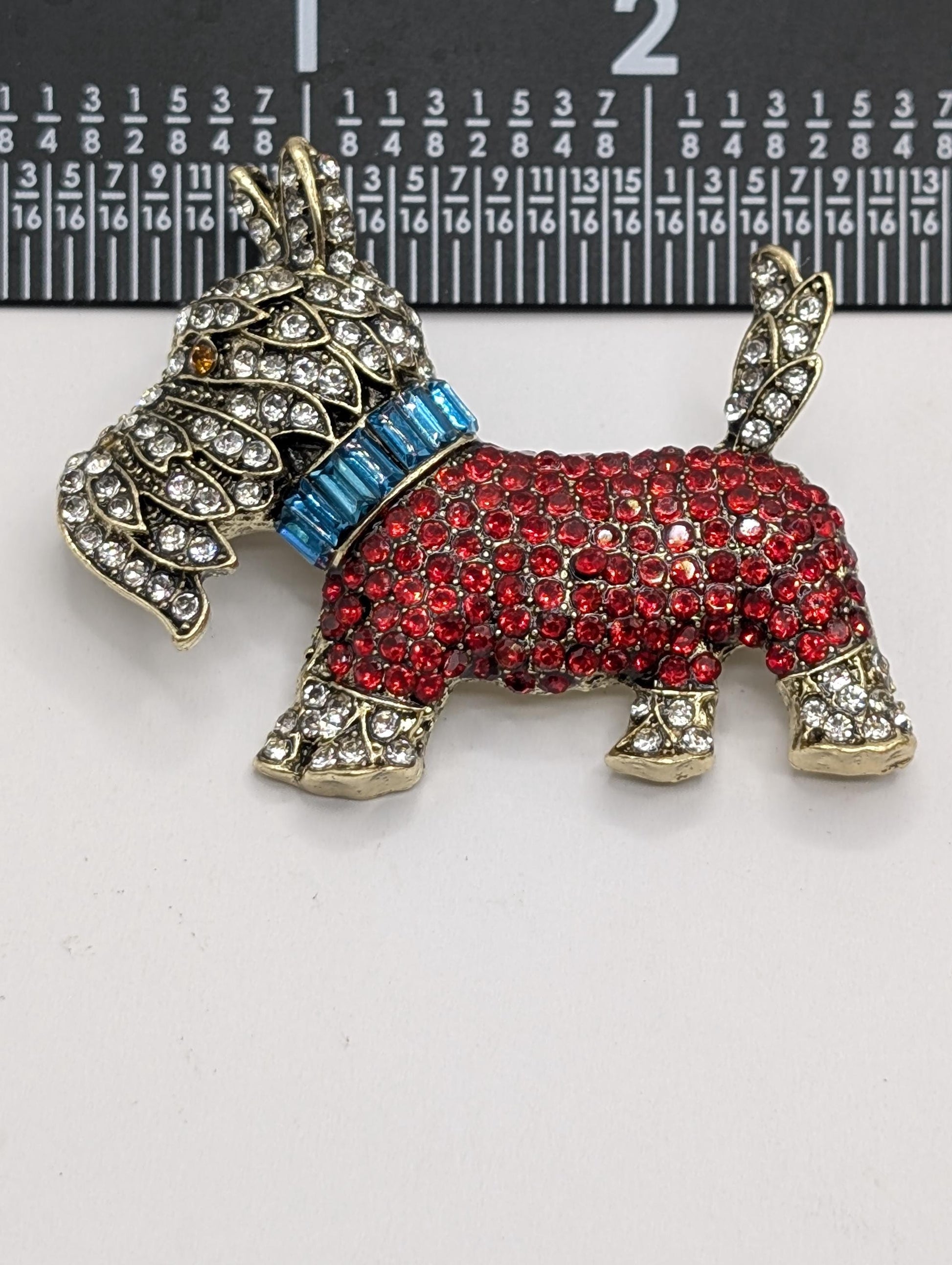 A decorative dog brooch made of red and gold materials, adorned with numerous sparkling rhinestones.