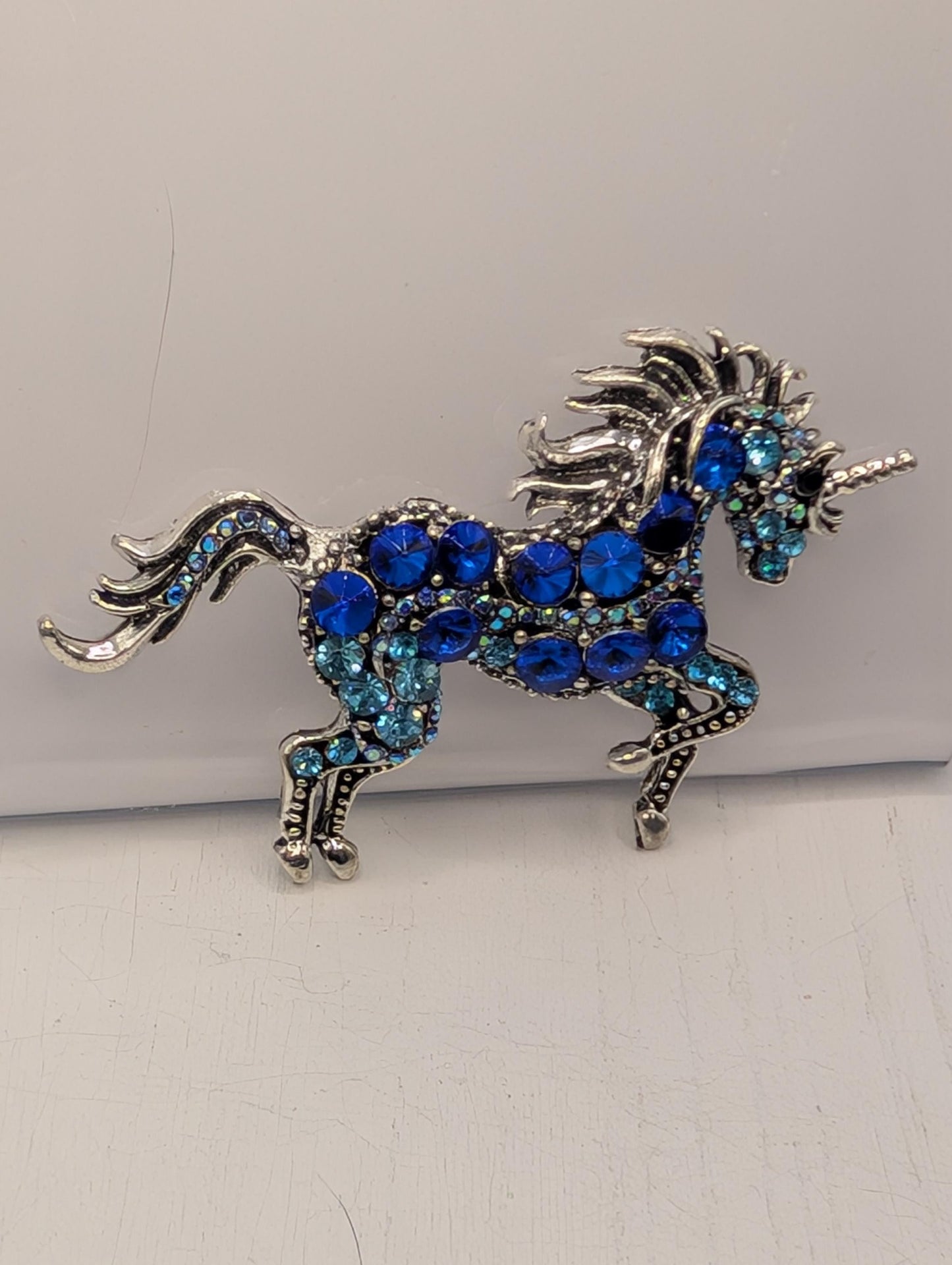 A decorative silver brooch in the shape of a unicorn, adorned with blue gemstones.