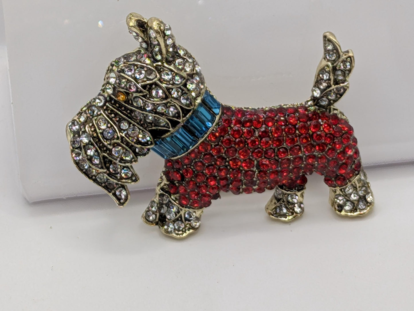 A decorative dog brooch made of red and gold materials, adorned with numerous sparkling rhinestones.