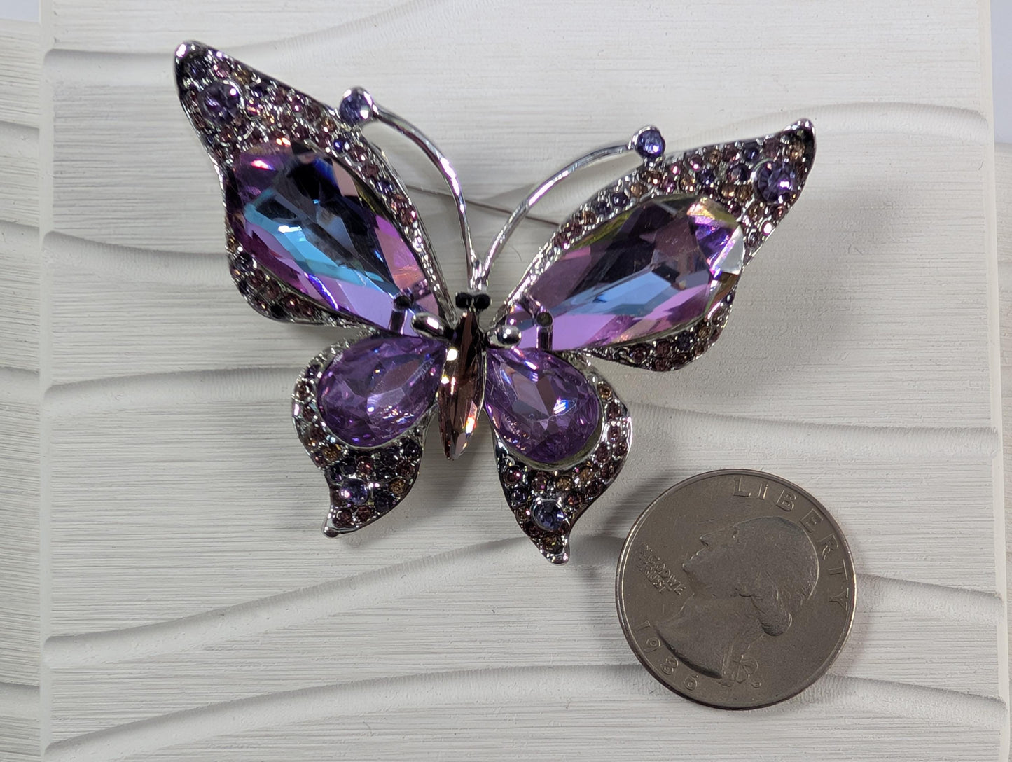 A decorative butterfly brooch with purple gemstones is placed next to a United States quarter.