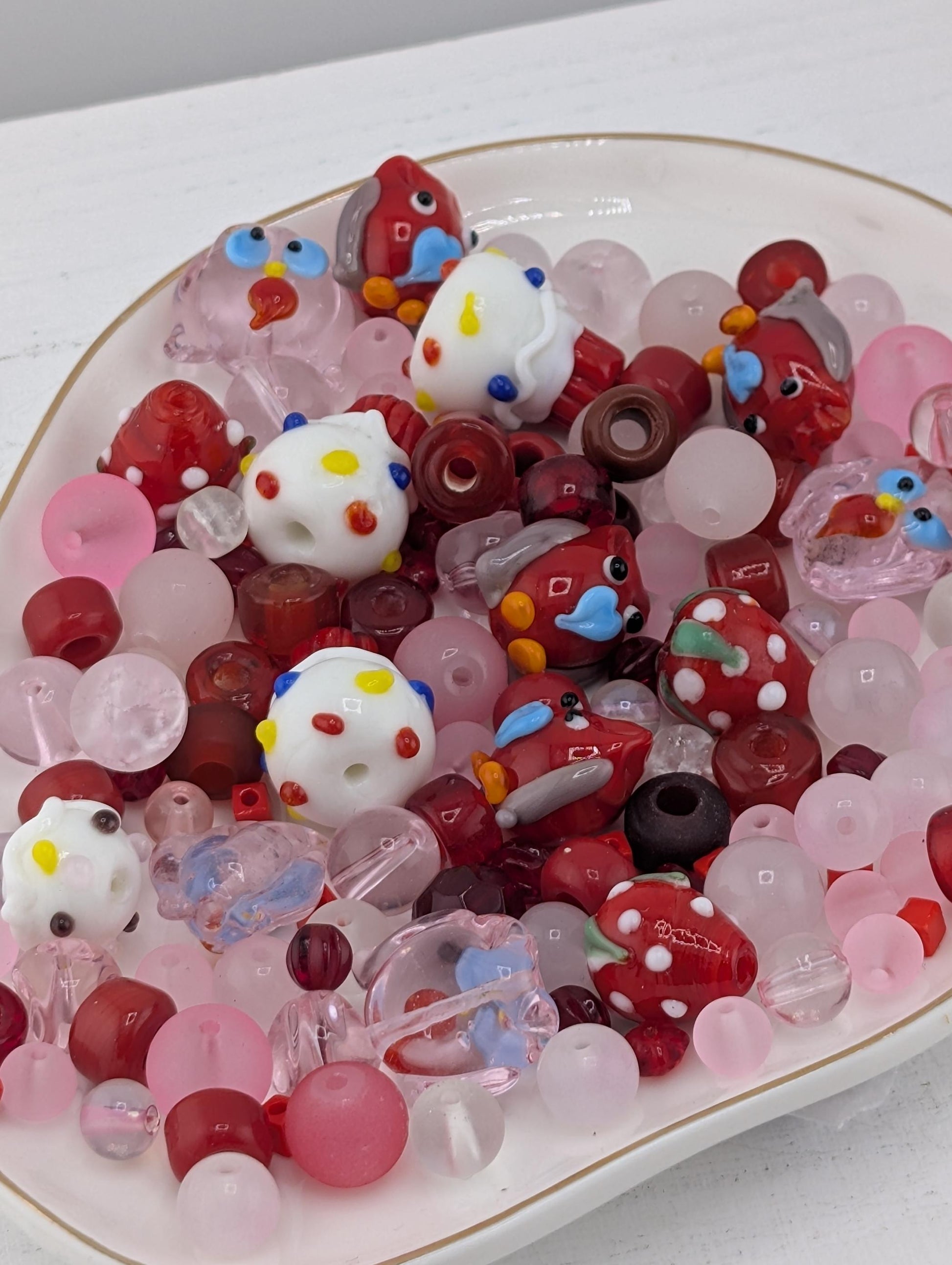 A white plate filled with a variety of colorful beads, including red, white, and pink beads, as well as some with polka dots and other playful designs.